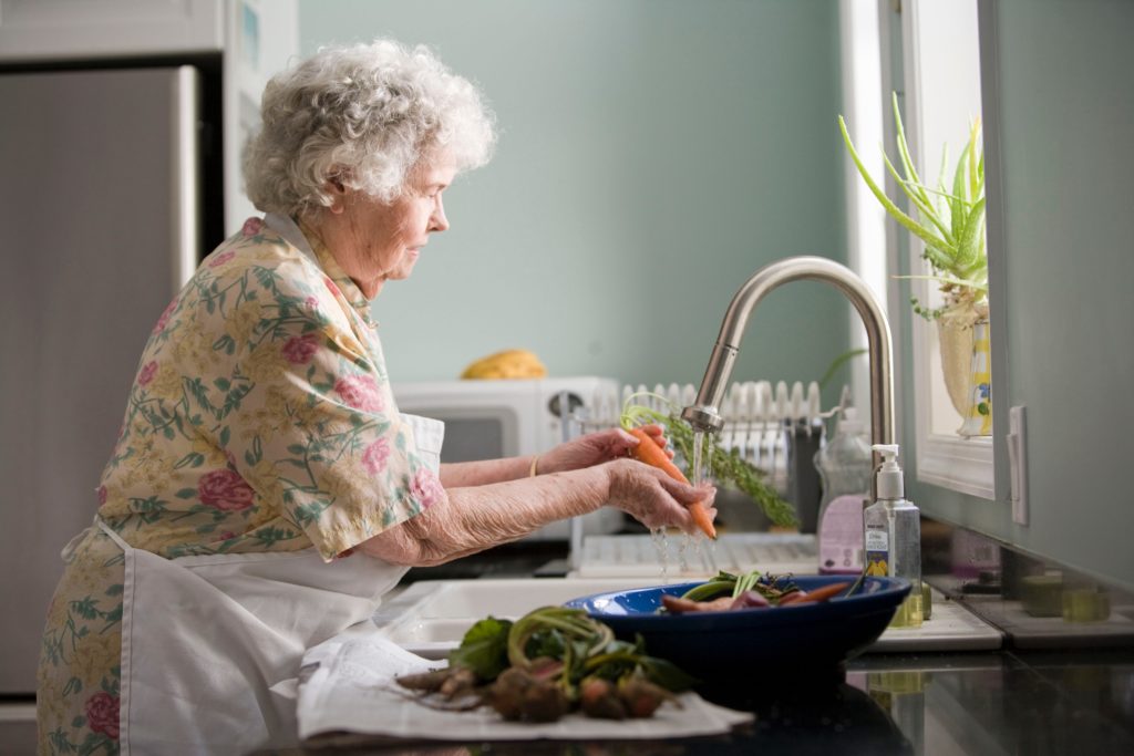 A socially isolated senior during COVID-19 pandemic washing vegetables at her kitchen sink
