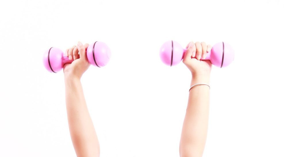 Arms of a senior reaching up while holding pink dumbbells for exercise